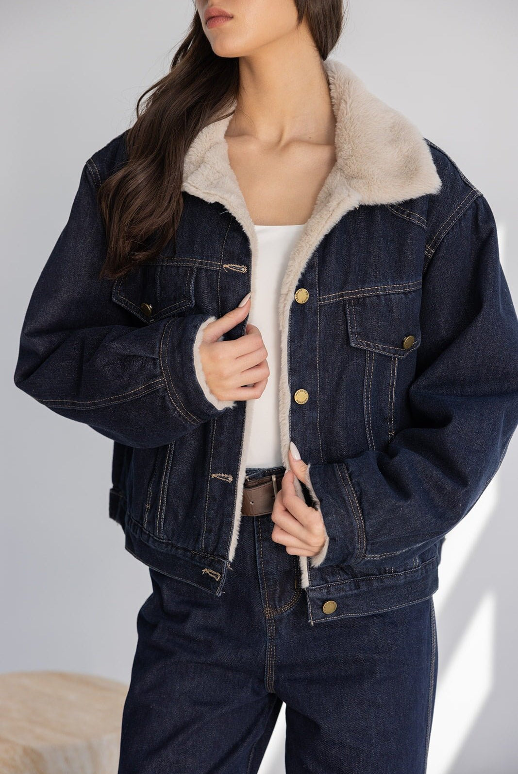 אישה לובשת ג'קט ג'ינס מרופד לנשים עם צווארון פרווה בצבע בז' ומכנסי ג'ינס כהים