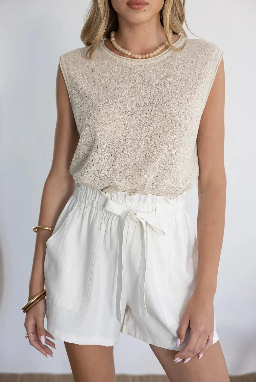 אישה לובשת גופיית בז' ושורטס קיץ לבנים עם קשירה, אופנת נשים קיץ