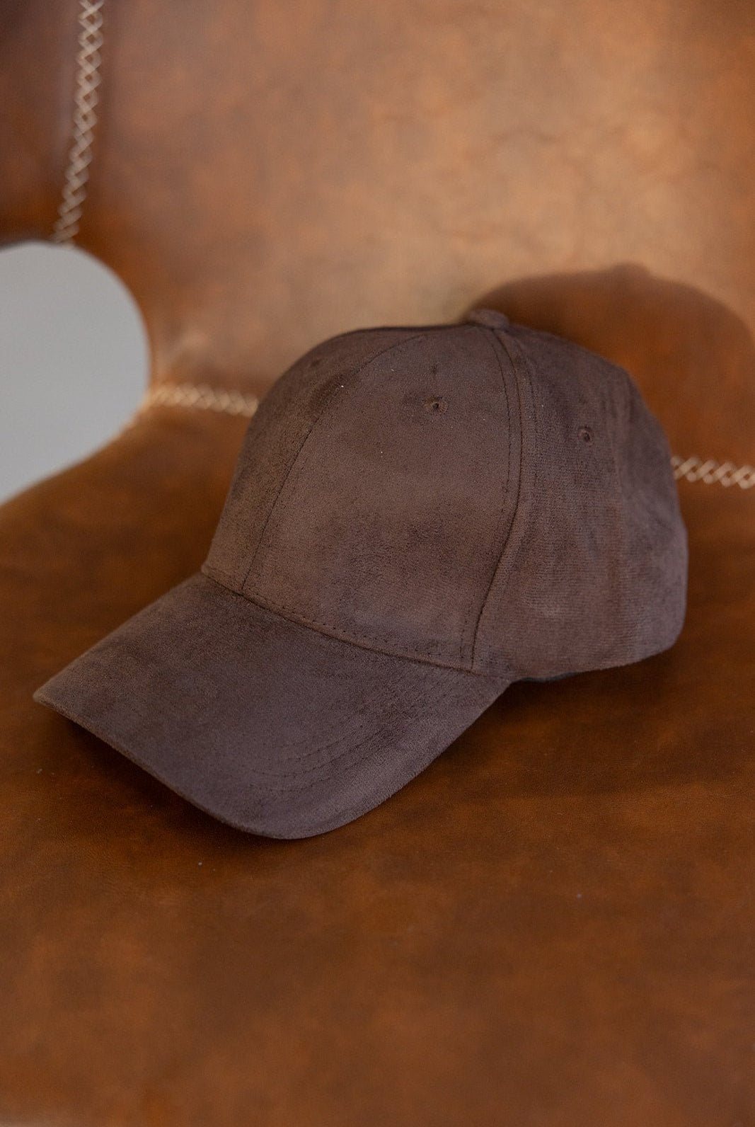 כובע מצחייה חום מבד זמש, מונח על כיסא עור חום, אופנת נשים ונערות