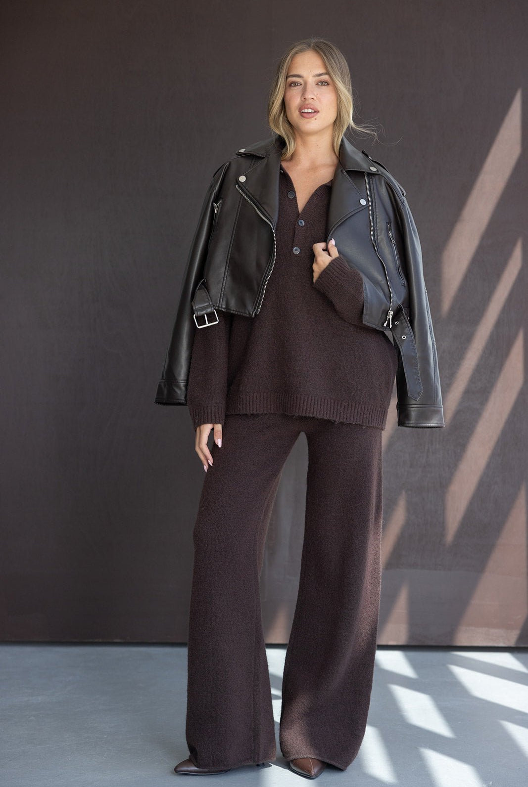 אישה לובשת חליפת טריקו חומה רחבה עם ג’קט דמוי עור שחור, אופנת נשים חורף