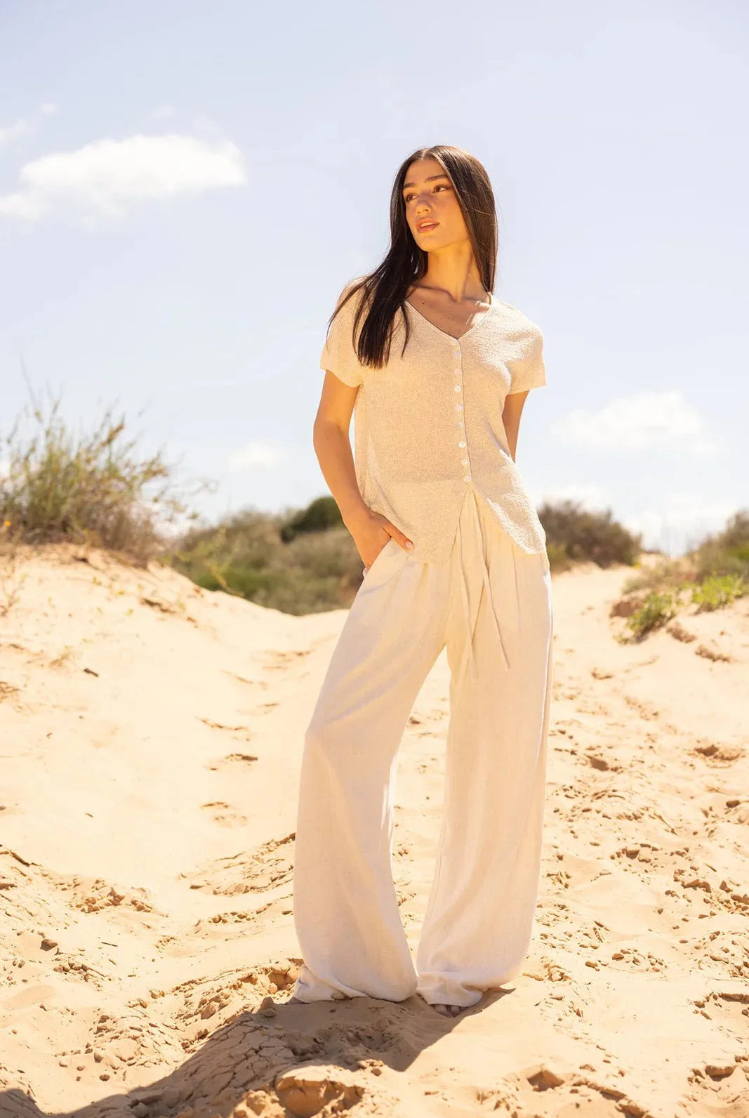 אישה עם חולצה קצרה ומכנסיים בלבן קייצי, על דיונה בשמש, אופנה לנשים צעירות