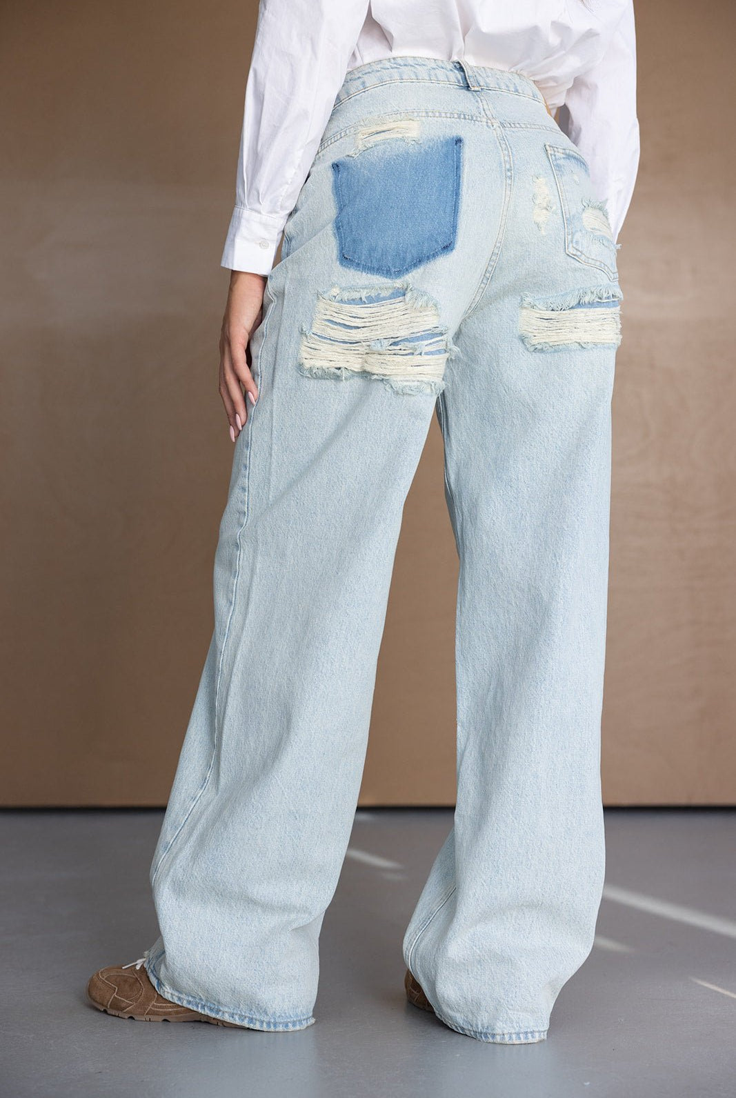 ג'ינס רחב בגזרת אוברסייז לנשים, בדנים בהיר עם קרעים וכיס אחורי כחול בולט, לוק אופנתי לנערות