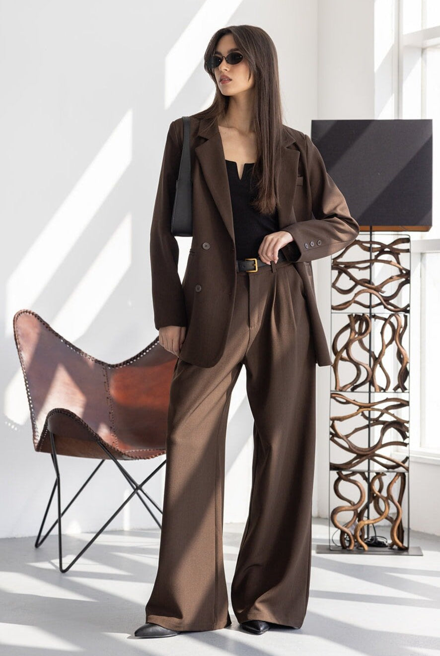 דוגמנית לובשת חליפה חומה לנשים, משקפי שמש, תיק שחור, באווירה מודרנית ומוארת