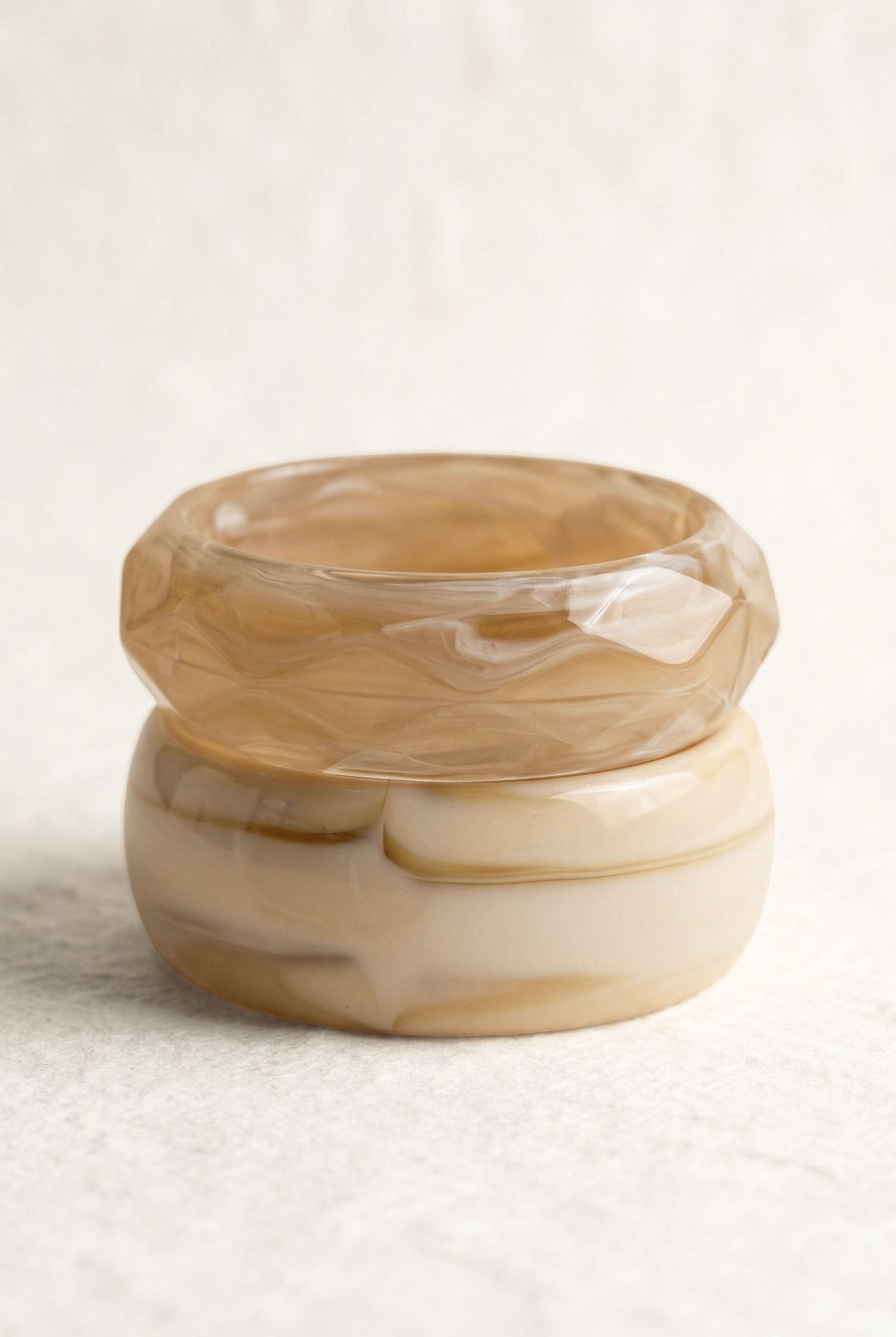 אישה עם תיק ורוד קלוע, לובשת וסט סרוג צבעוני ומכנסיים לבנים, עומדת ליד חלון מואר