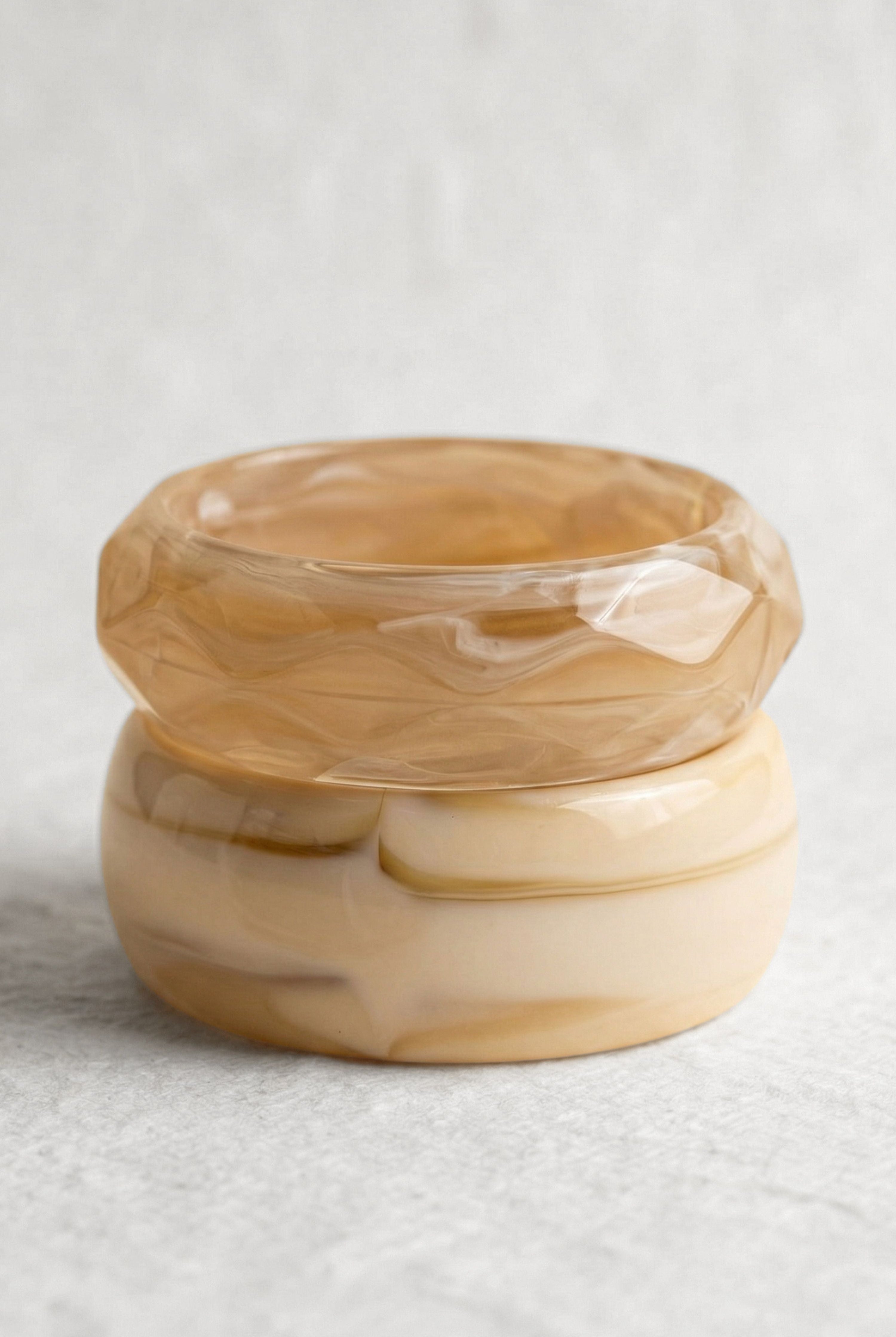 אישה עם תיק ורוד קלוע, לובשת וסט סרוג צבעוני ומכנסיים לבנים, עומדת ליד חלון מואר