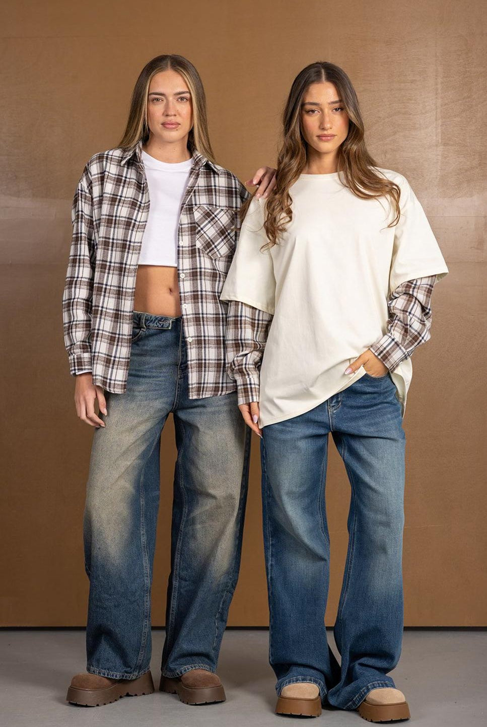 שתי נשים בבגדי אופנה יומיומית, חולצות משובצות ומכנסי ג'ינס רחבים, רקע חום