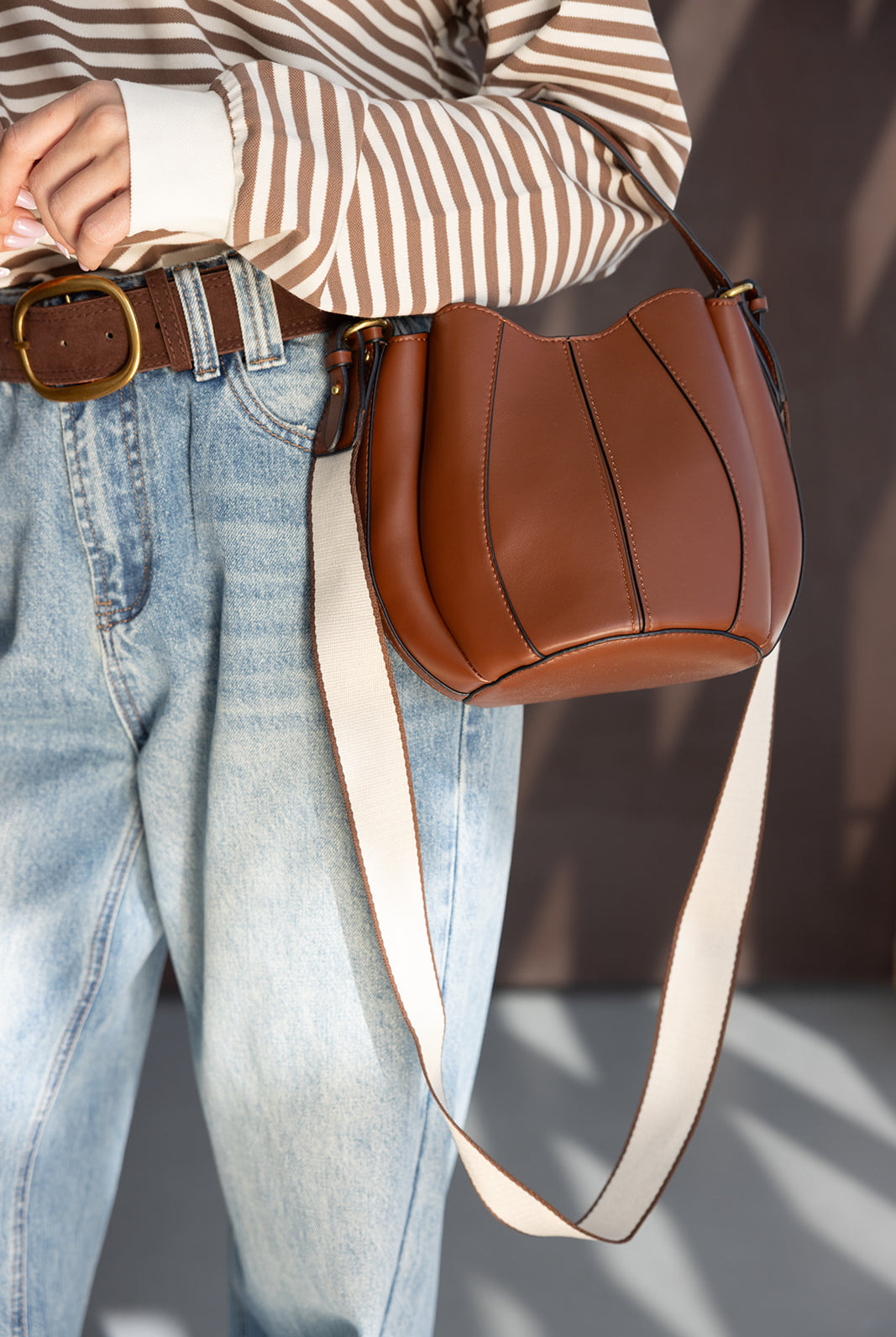 תיק צד חום מעור עם רצועה רחבה, חולצת סטריפס חומה וג’ינס בגזרה גבוהה לאופנת נשים