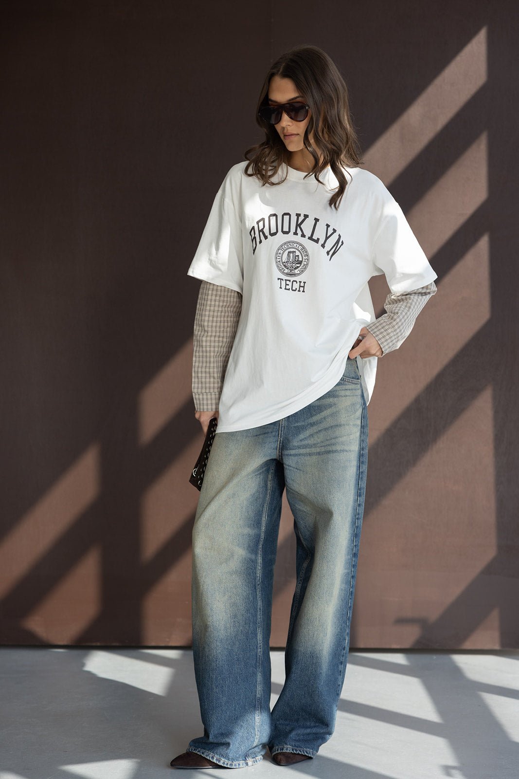אישה עם חולצת טי לבנה BROOKLYN TECH, מכנסי ג'ינס רחבים ואביזרי אופנה, מראה קז'ואל טרנדי לנשים