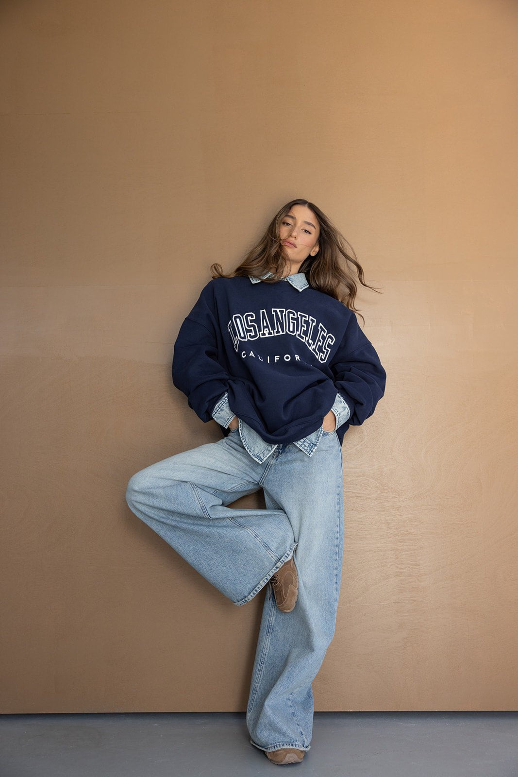 דוגמנית עם סווטשירט כחול כהה עם כיתוב LOS ANGELES ומכנסי ג'ינס רחבים, לוק קז'ואל אופנתי לנשים