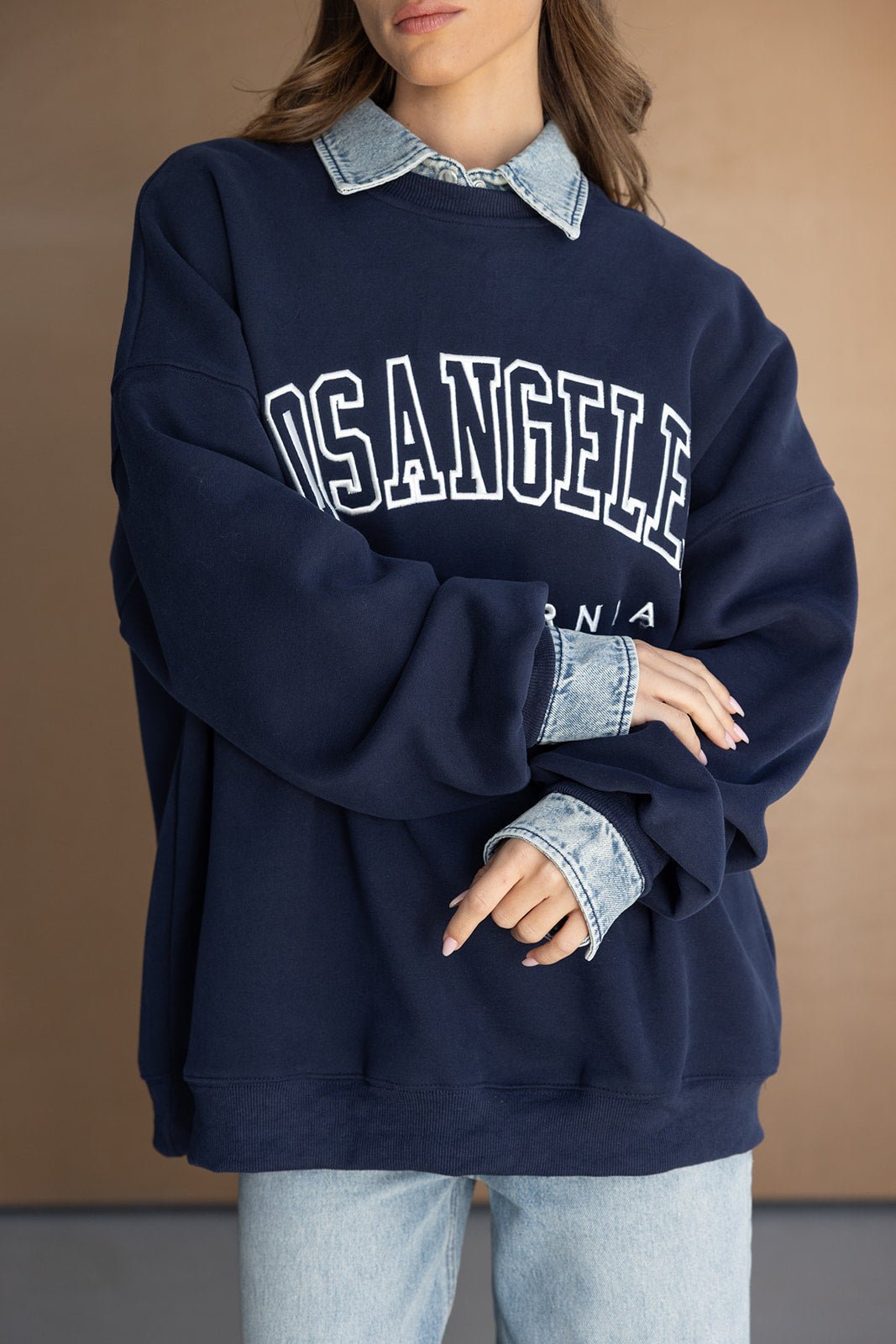 אישה לובשת סווטשרט כחול כהה עם כיתוב LOS ANGELES בשכבה על חולצת ג'ינס וג'ינס בהיר, אופנה לנערות