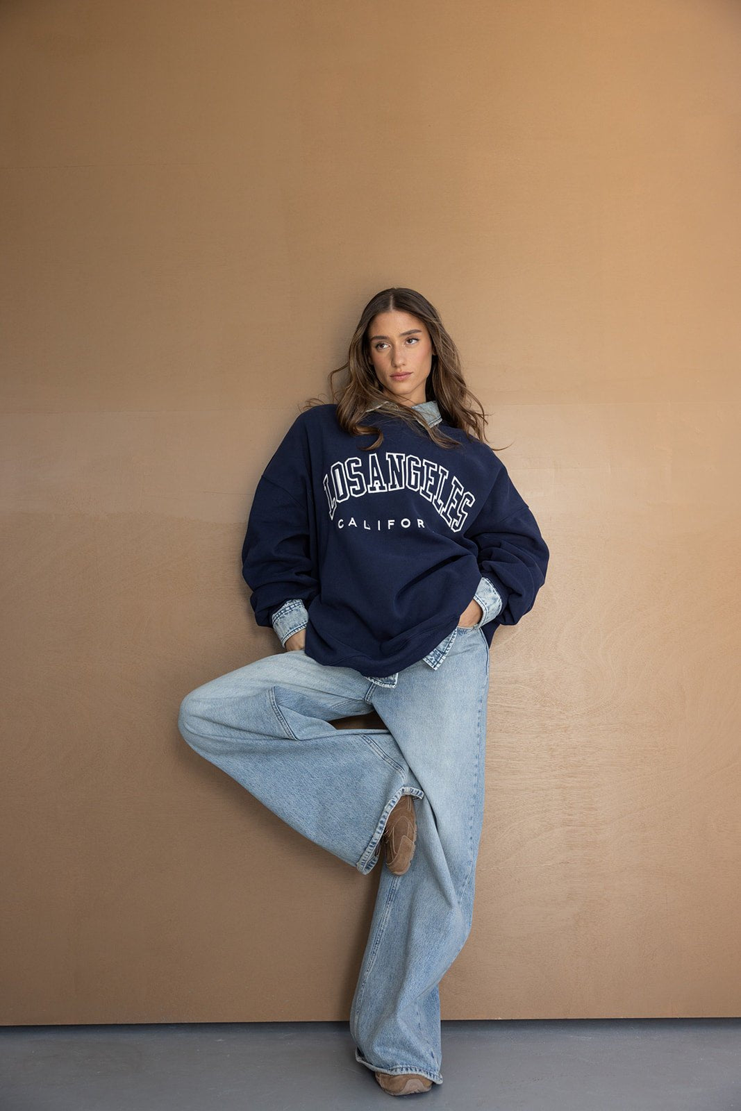 דוגמנית לובשת סווטשרט כחול עם כיתוב LOS ANGELES ומכנסי ג'ינס רחבים, אופנת נשים צעירה