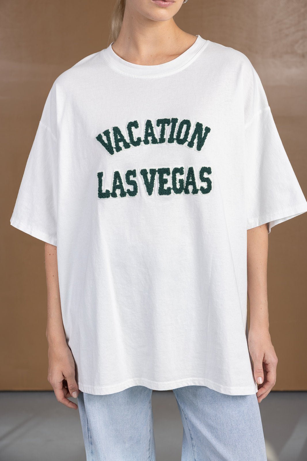 אישה בחולצת טי שירט לבנה עם הכיתוב 'VACATION LAS VEGAS' ומכנסי ג'ינס קז'ואל