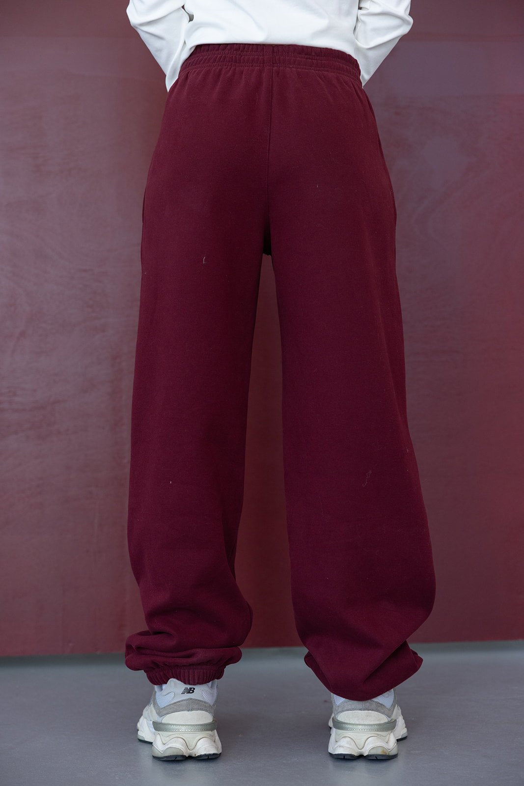 מכנסי טרנינג בורדו לנשים, גזרה רחבה ובד נעים, מצולמים מאחור, עם סניקרס לבנים