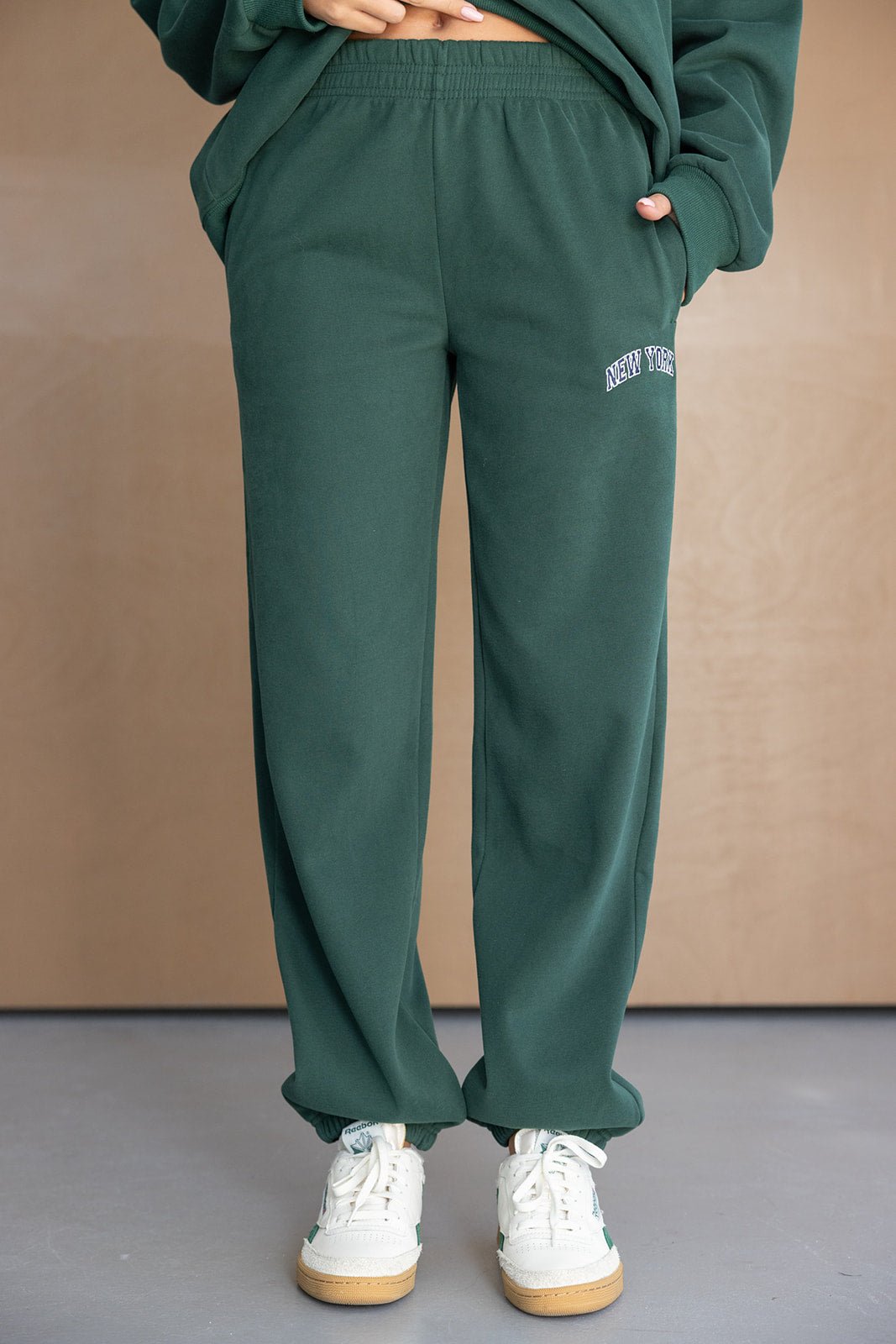 מכנסי טרנינג ירוקים לנשים עם גומי במותן, כיתוב NEW YORK, מראה קז'ואל אופנתי.