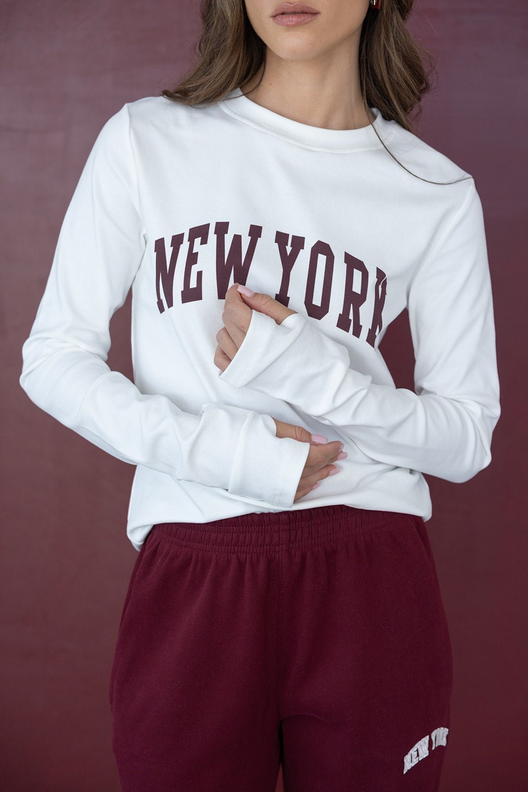 אישה לובשת חולצת טרנינג לבנה עם כיתוב NEW YORK ומכנסי טרנינג בורדו אופנתיים