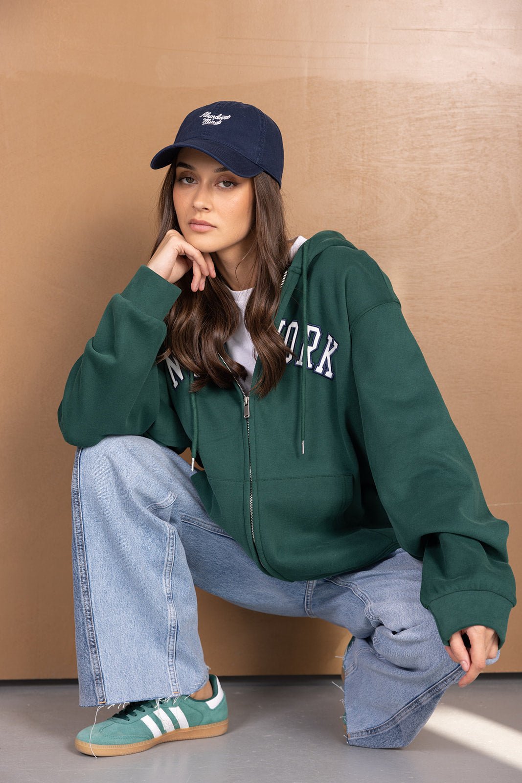 דוגמנית עם קפוצ׳ון ירוק, כובע כחול, ג׳ינס רחב ונעלי ספורט ירוקות, אופנת רחוב לנשים