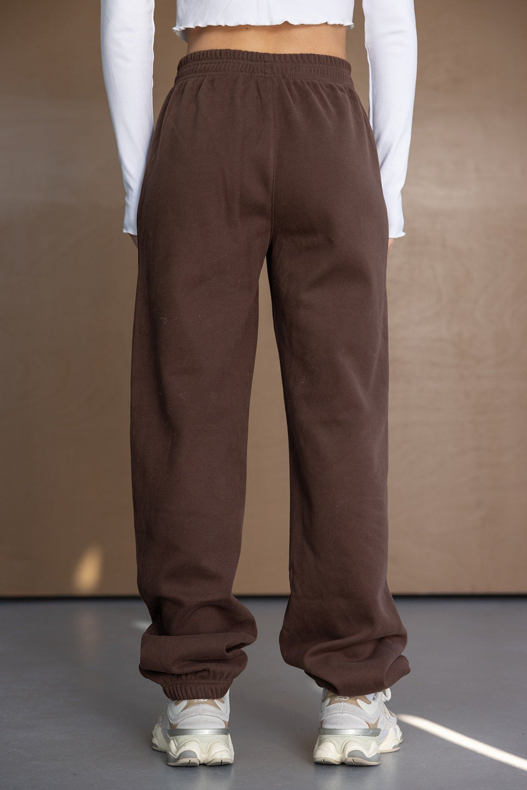 מכנסי טרנינג חומים לנשים, גזרה רחבה, בד נוח, תצוגה על דוגמנית עם חולצה לבנה ונעליים ספורט