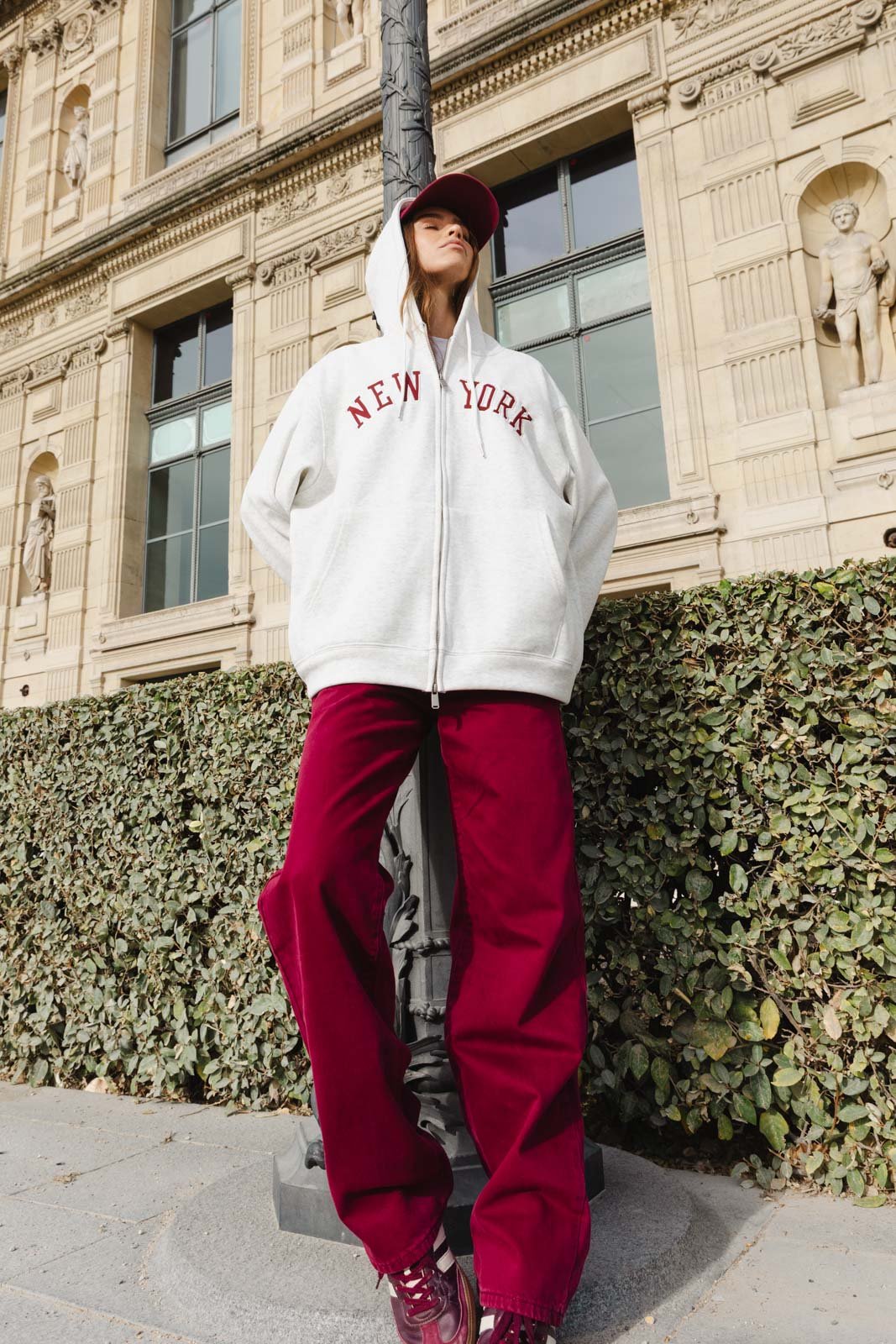 אופנת רחוב לנשים, דוגמנית עם קפוצ׳ון אפור NEW YORK ומכנסיים בורדו, לוק קז׳ואלי עירוני