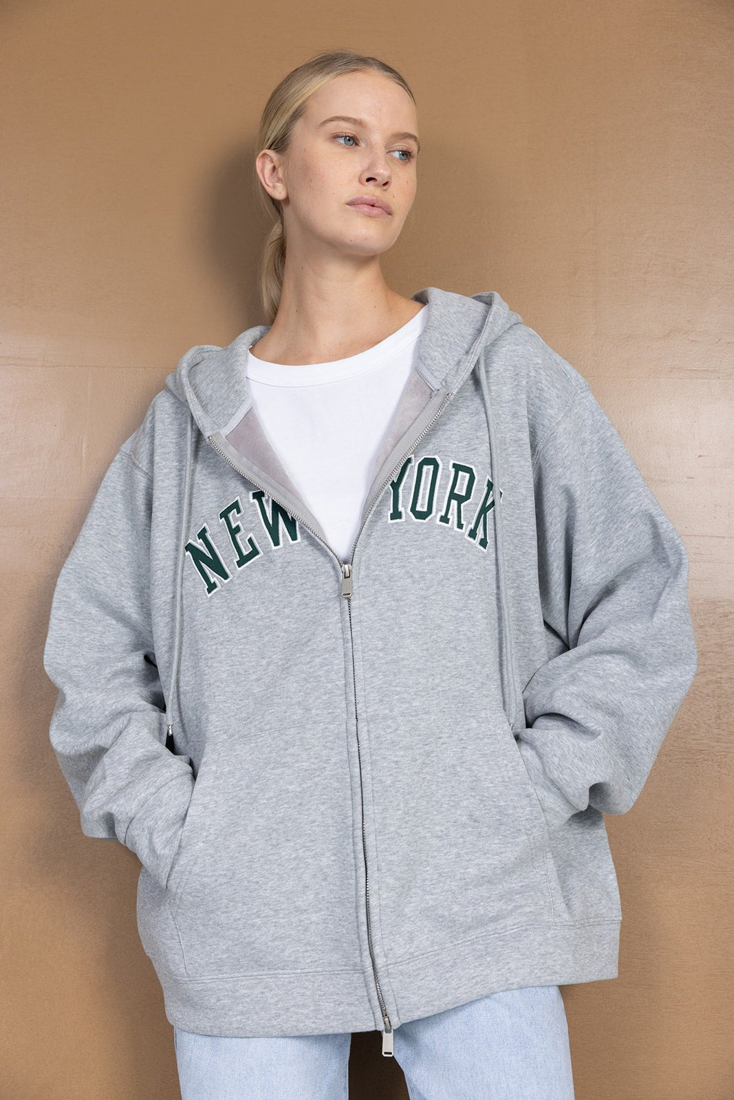 דוגמנית לובשת קפוצ׳ון אפור עם רוכסן וכיתוב ניו יורק, אופנת נשים ונערות