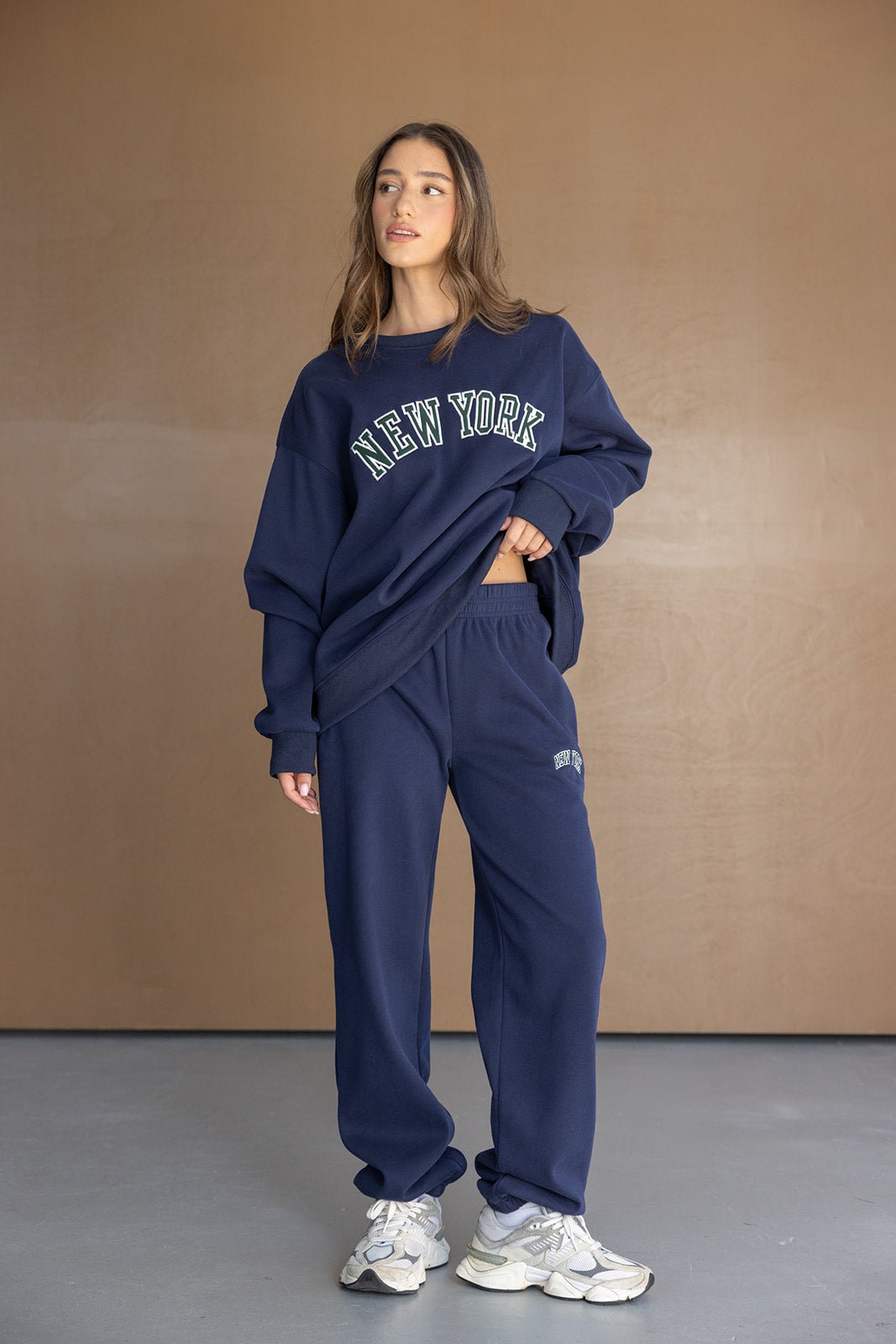 דוגמנית לובשת סט טרנינג נשים כחול כהה עם כיתוב NEW YORK, אופנת רחוב צעירה ונעלי סניקרס