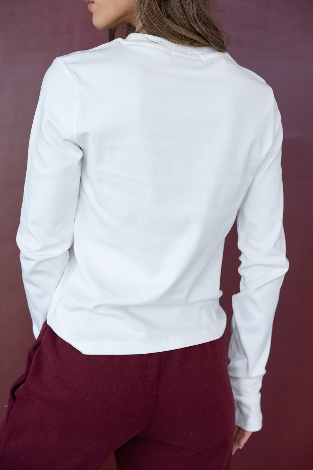 אישה לובשת חולצה לבנה ארוכה ומכנסיים בורדו, צילום גב, אופנה לנשים
