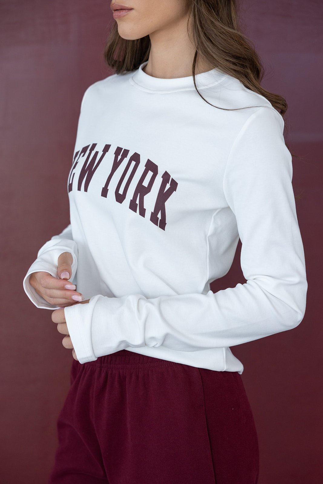 דוגמנית לובשת סווטשירט לבן עם הכיתוב NEW YORK ומכנסי טרנינג בורדו, אופנת נשים קז'ואל