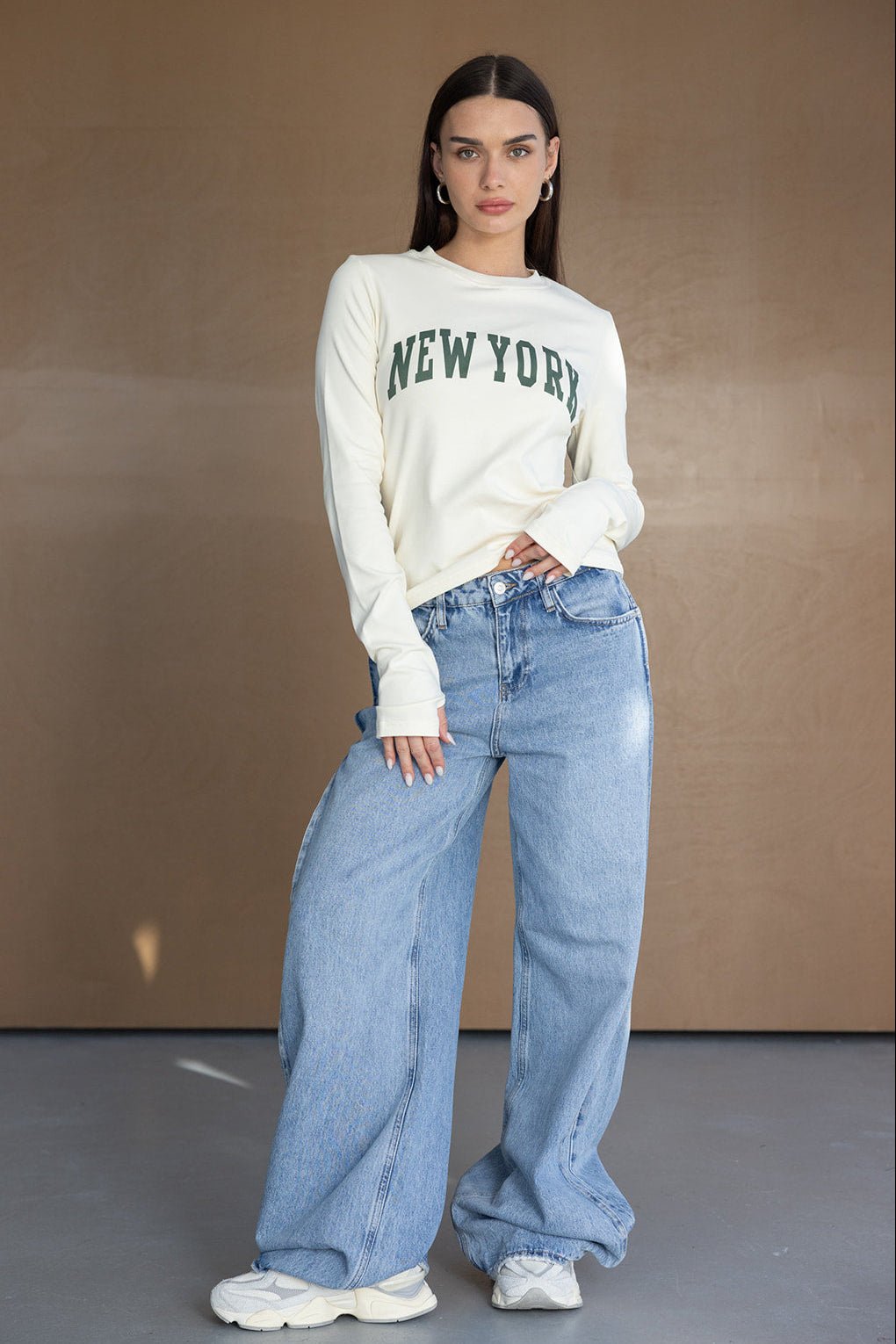 דוגמנית לובשת חולצה לבנה עם כיתוב NEW YORK, ג'ינס רחב ונעלי סניקרס אופנתיות, אופנה לנשים צעירות