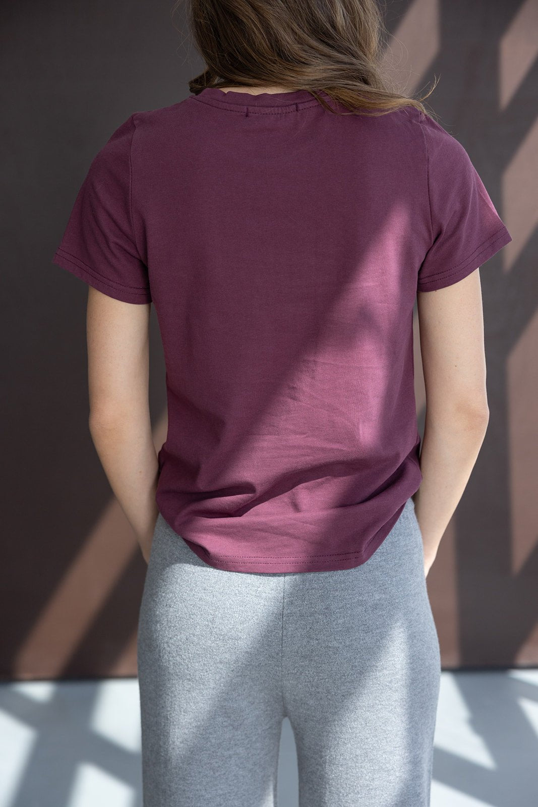 אישה לובשת חולצת טי בורדו ומכנסיים אפורים באווירה מודרנית, בגדי אופנה לנשים