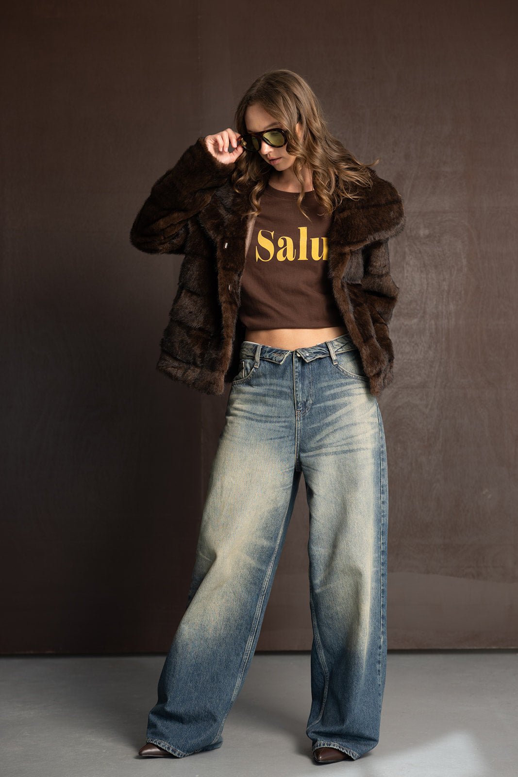 אישה עם חולצה חומה מודפסת, מעיל פרווה חום ומכנסי ג'ינס רחבים, אופנה לנשים צעירות