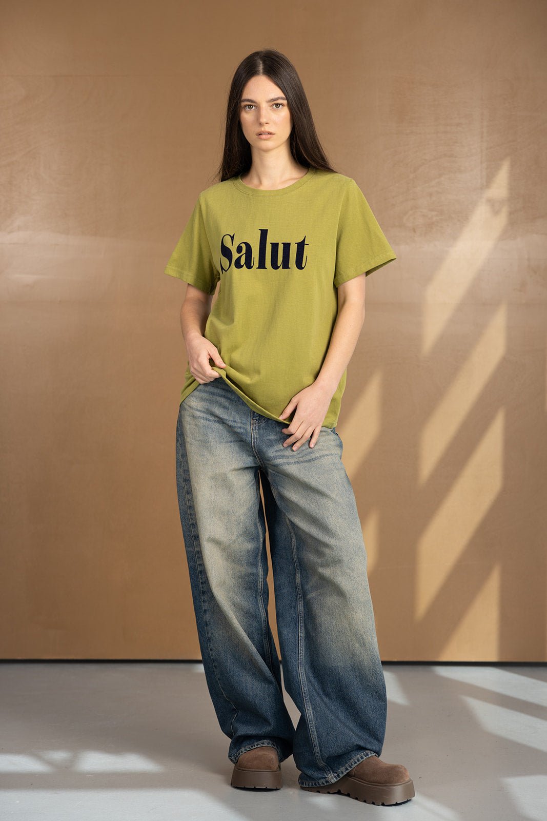 אישה לובשת טי שירט ירוק עם כיתוב Salut ומכנסי ג'ינס רחבים, אופנת נשים ונערות בסגנון יומיומי