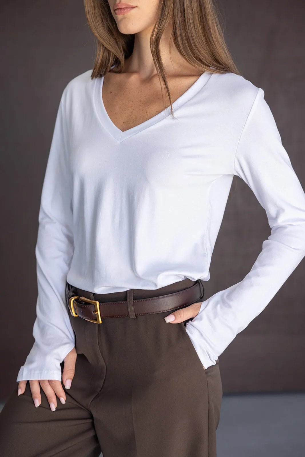 חולצת נשים לבנה ארוכה עם מחשוף וי, מכנסיים חומים עם חגורה, מראה אופנתי צעיר