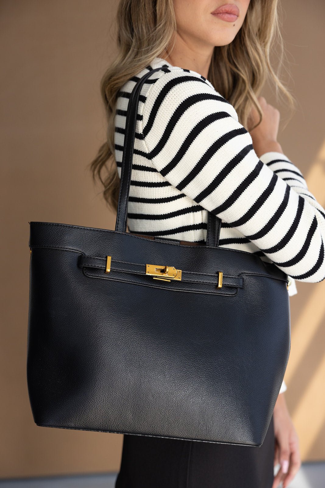 אישה עם סוודר פסים מחזיקה תיק צד גדול עור שחור עם אבזם זהב, אופנת נשים אלגנטית