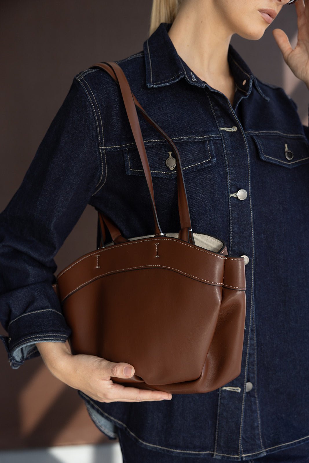 אישה עם ג'קט ג'ינס מחזיקה תיק כתף חום אופנתי לנשים, צילום מקרוב