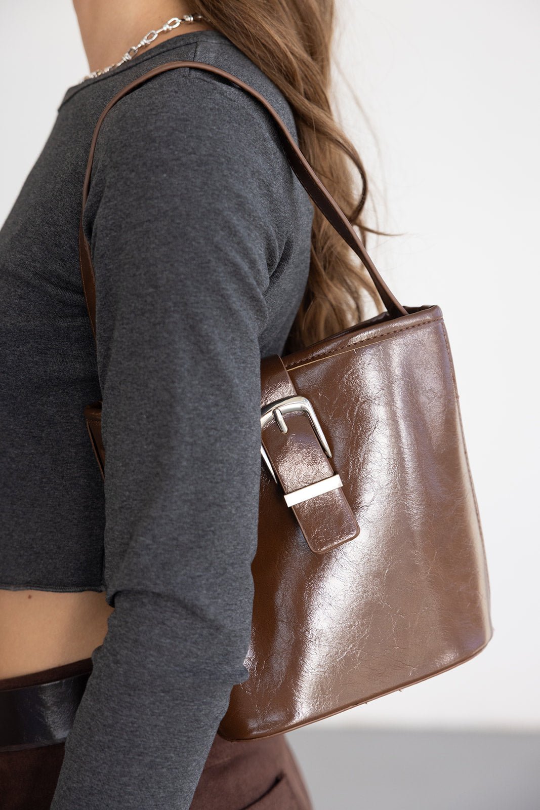 תיק כתף חום מעור עם אבזם כסוף אופנתי על כתף של אישה, לוק קז'ואל לנשים