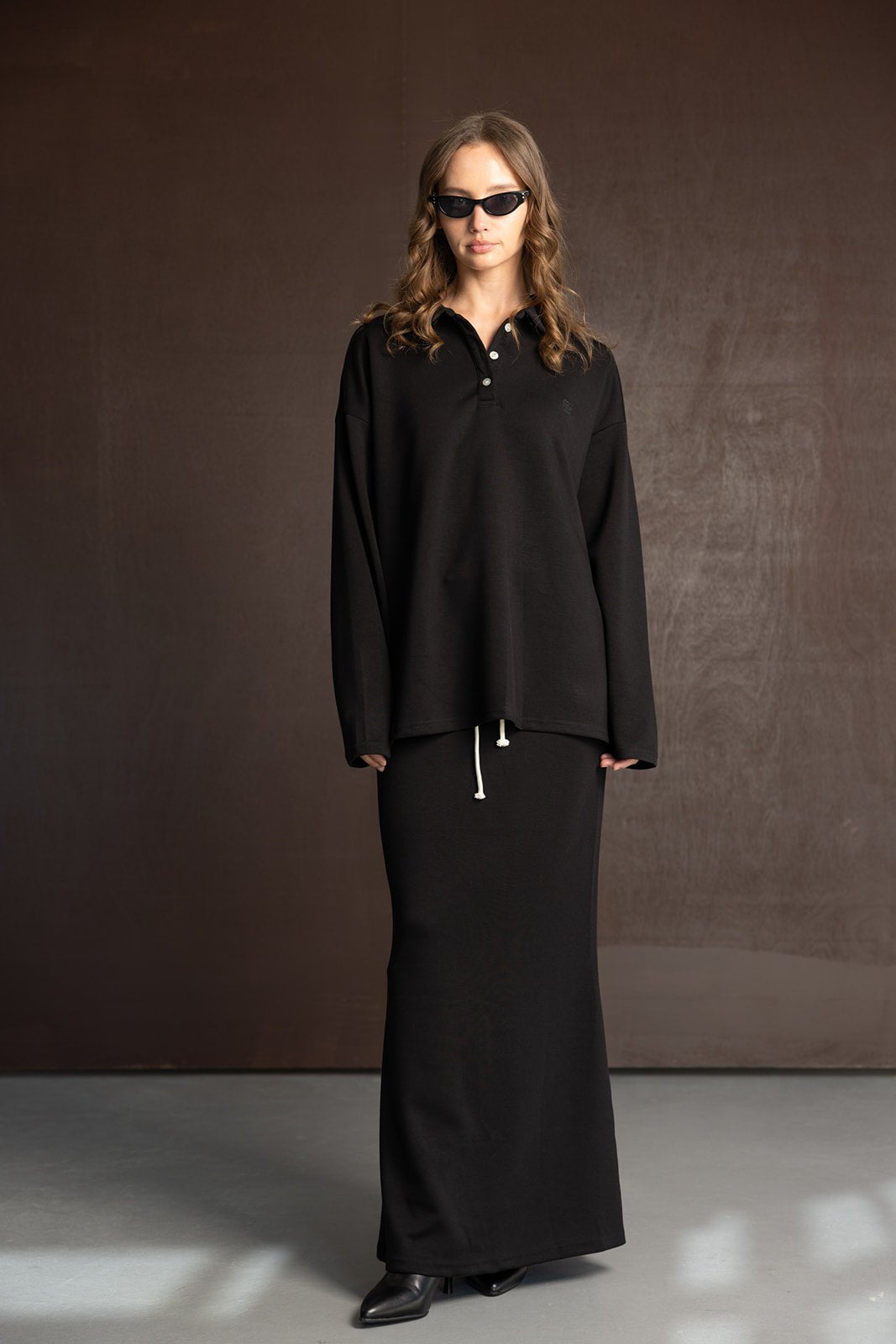דוגמנית עם חולצה שחורה בשרוול ארוך וחצאית שחורה ארוכה, לוק אופנתי לנשים