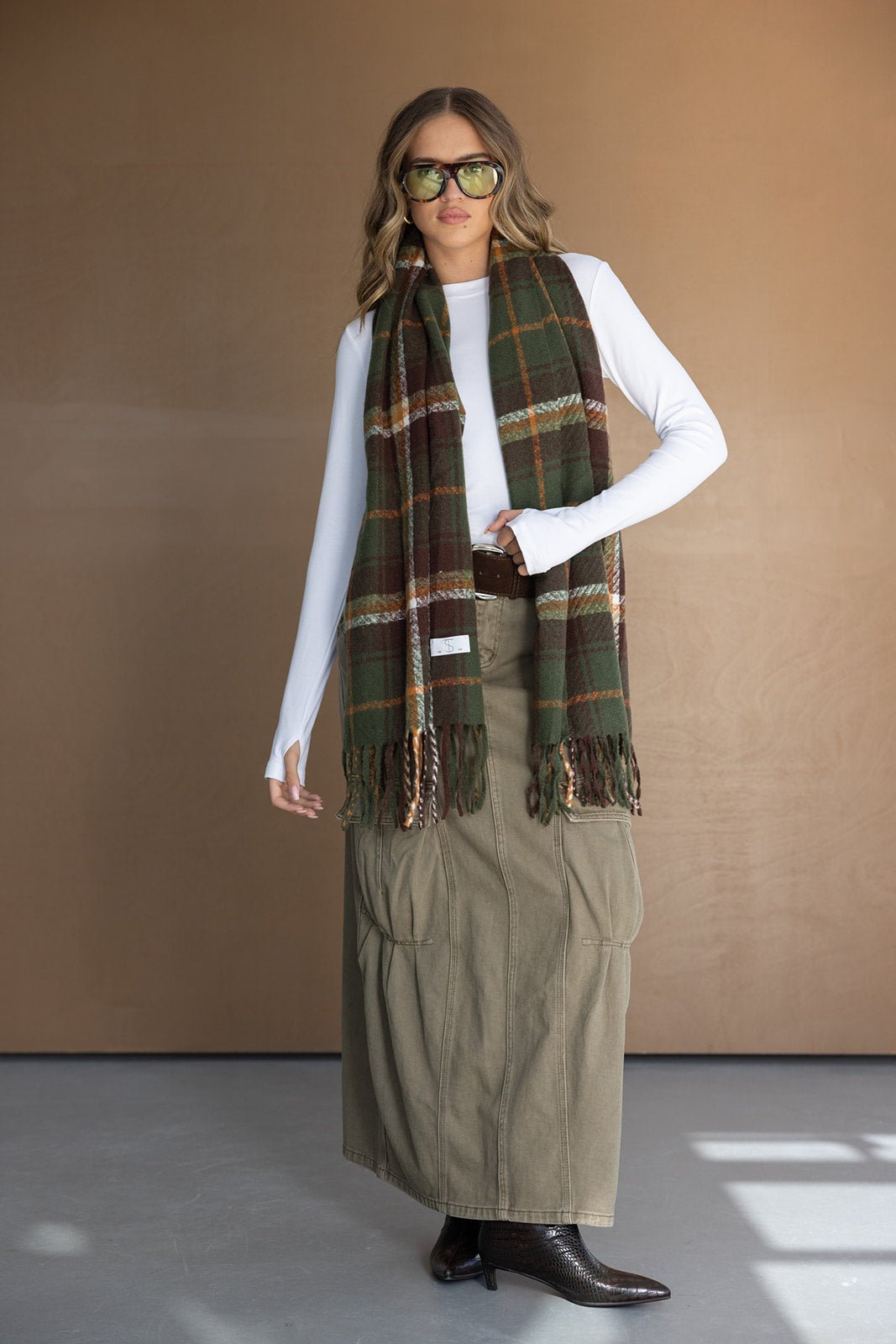 אופנת חורף לנשים: דוגמנית עם צעיף משובץ ירוק-חום, חולצה לבנה וחצאית ירוקה ארוכה