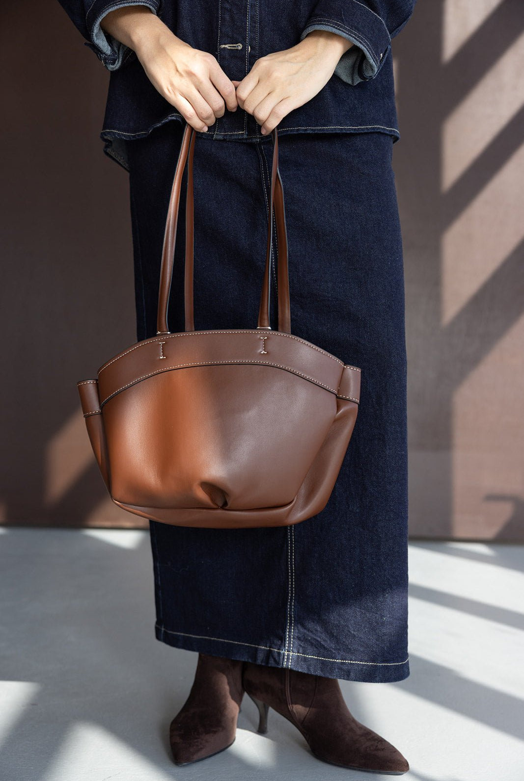 תיק נשי חום מעור עם ידיות ארוכות, לבוש ג'ינס ומגפונים חומים, אופנה לנשים