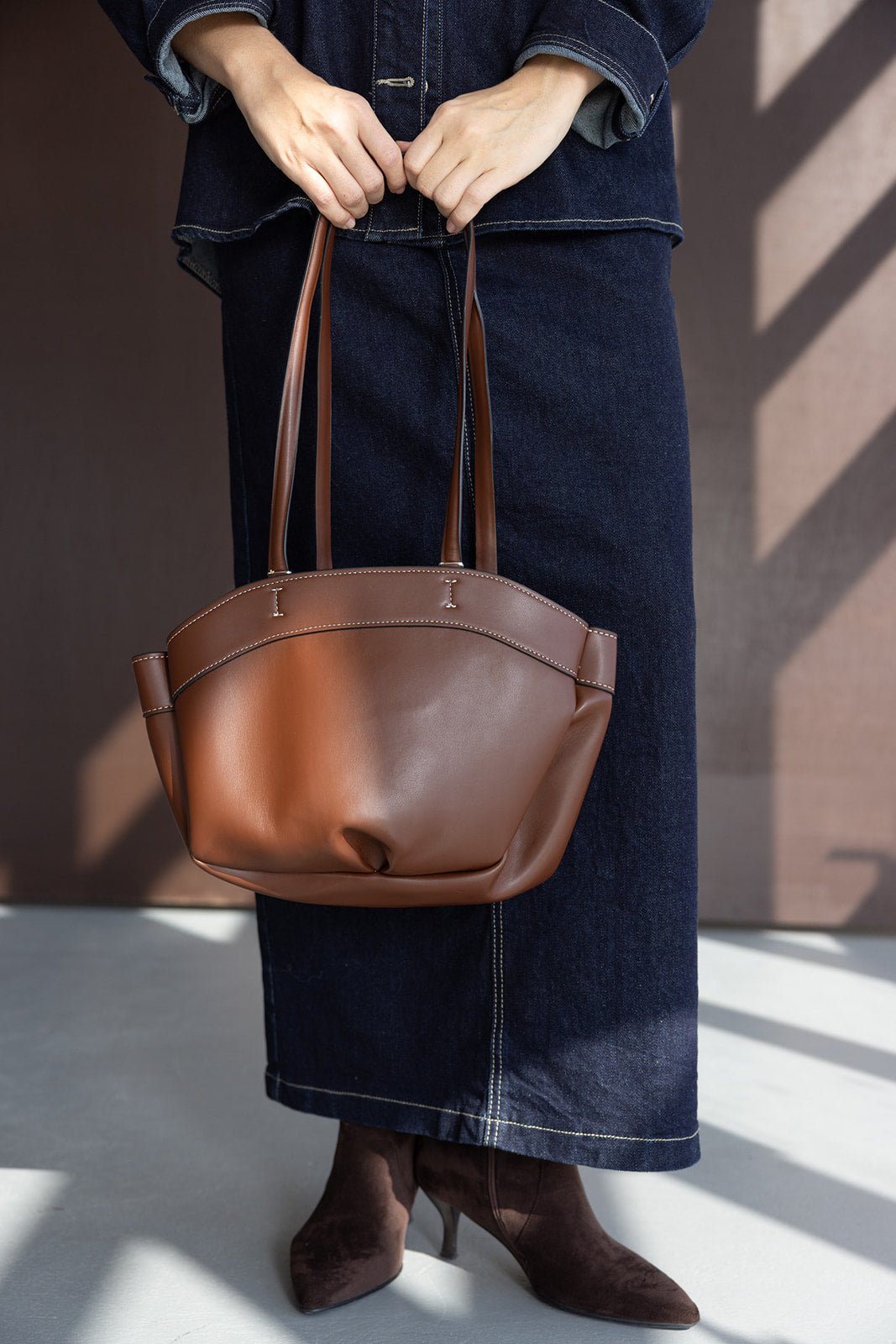 תיק נשי חום מעור עם ידיות ארוכות, לבוש ג'ינס ומגפונים חומים, אופנה לנשים