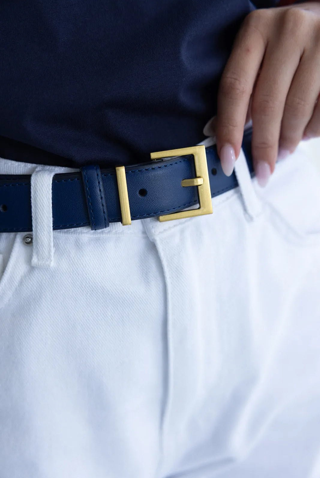 חגורת עור כחולה עם אבזם זהב על מכנסי ג'ינס לבנים, אופנת נשים קיץ 2024