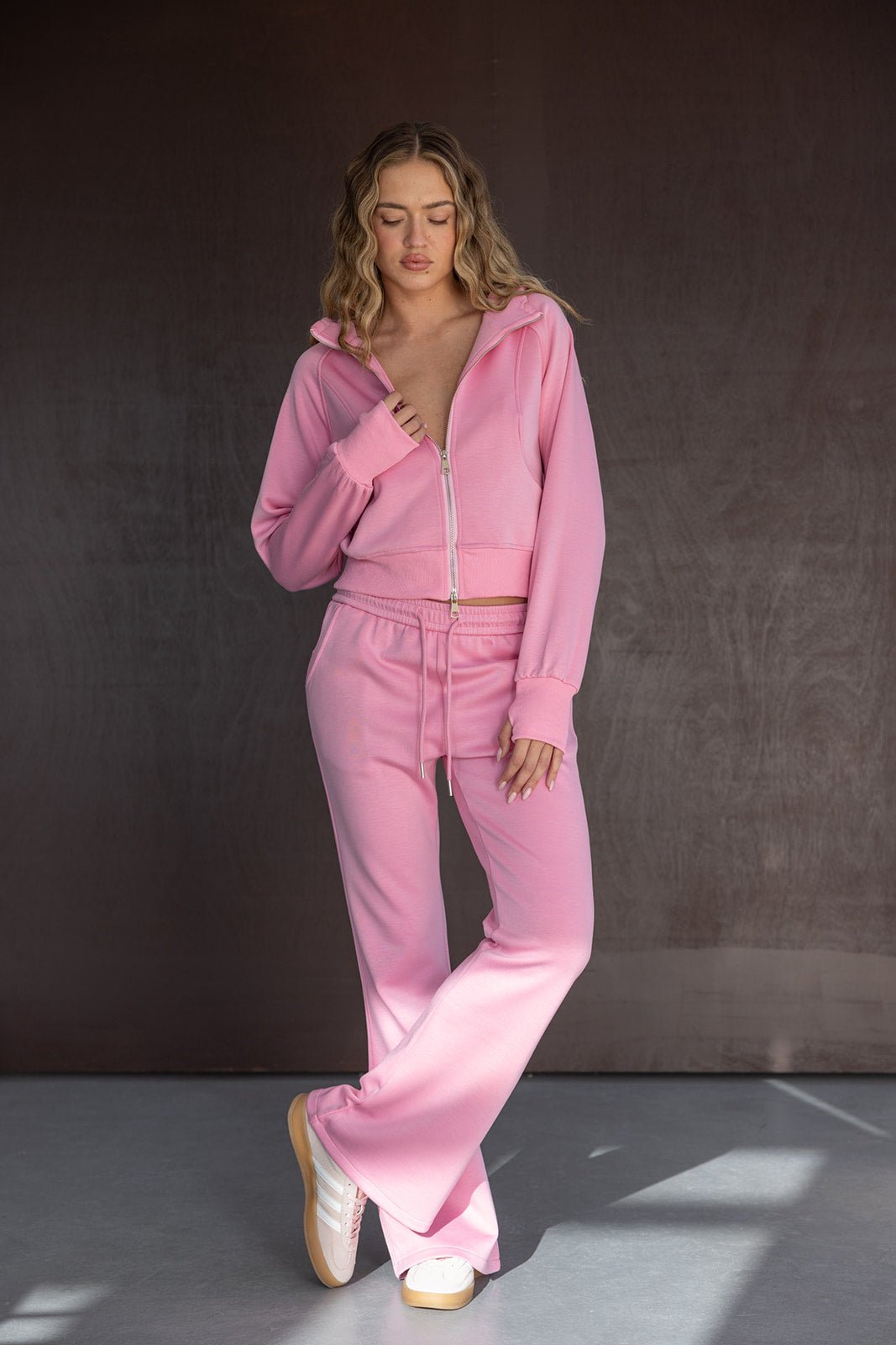 דוגמנית לובשת סט טרנינג ורוד עם קפוצ׳ון וריצ׳רץ׳, מכנסיים רחבים ונעלי סניקרס, אופנת נשים קז׳ואל