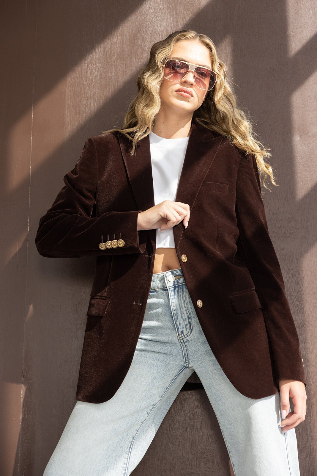 אישה עם בלייזר קטיפה חום, טי שירט לבנה וג'ינס גבוה, משקפי שמש אופנתיים