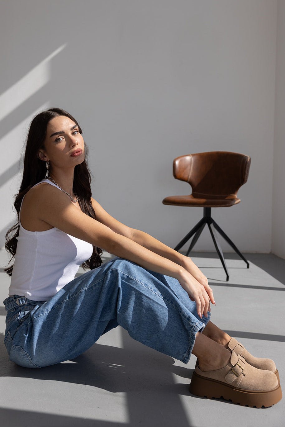 דוגמנית יושבת על הרצפה עם גופייה לבנה, ג'ינס רחב ונעלי פלטפורמה בז', אופנת נשים מודרנית