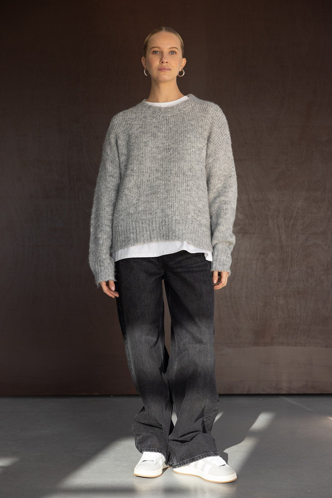 אישה לובשת סוודר אפור, ג'ינס שחור רחב ונעליים לבנות, אופנת חורף לנשים צעירות