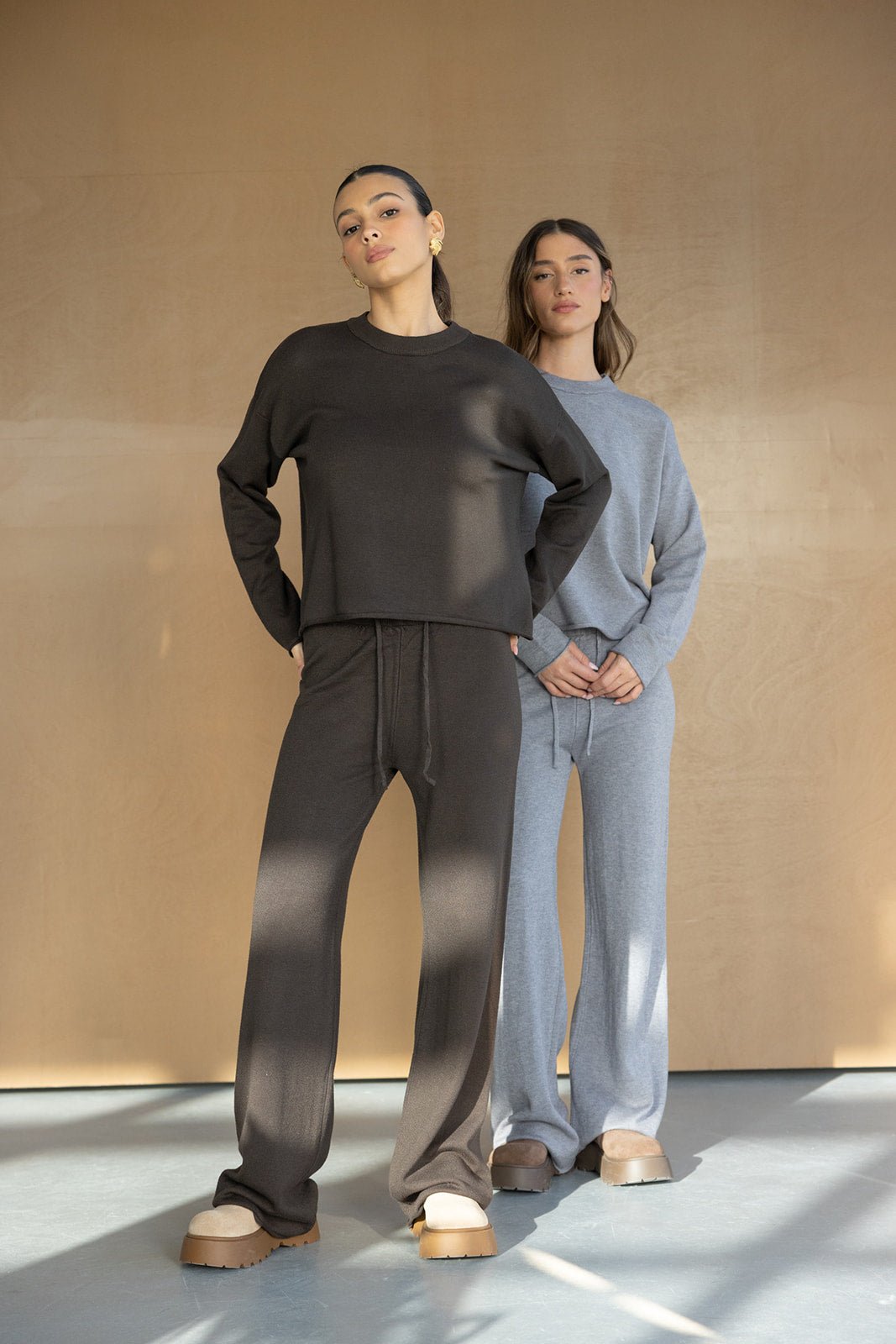 שתי נשים עם סט טרנינג אופנתי, אחת בצבע חום כהה ואחת באפור, לוק קז'ואל עכשווי.