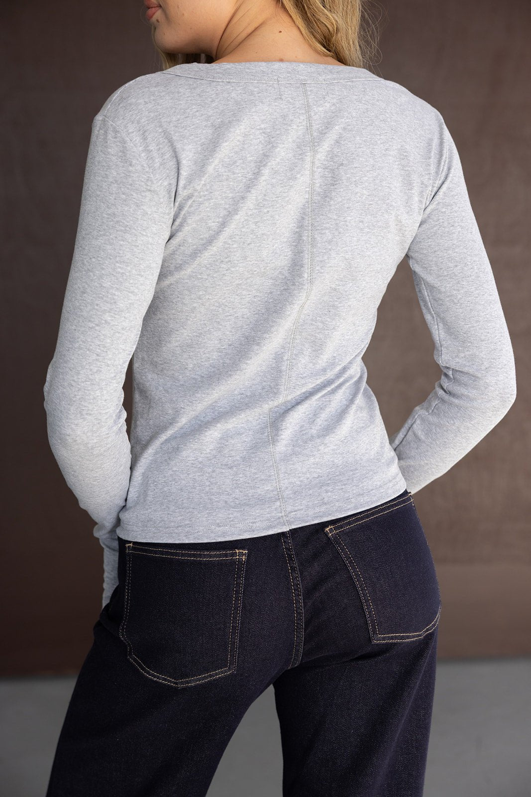 דוגמנית עם חולצה אפורה ארוכת שרוול ומכנסי ג'ינס כהים, צילום מאחור, אופנת נשים ונערות