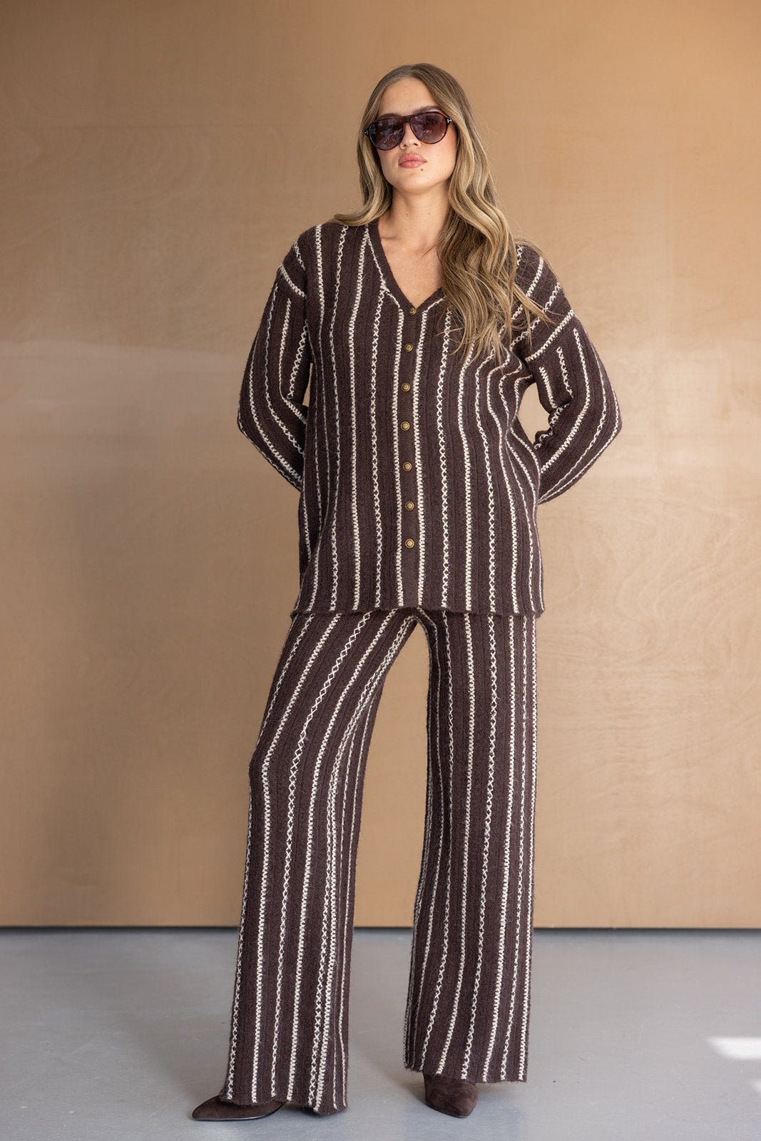 אישה עם משקפי שמש לובשת סט חורף חום עם פסים לבנים, חולצה ומכנסיים מחמיאים לאופנת נשים