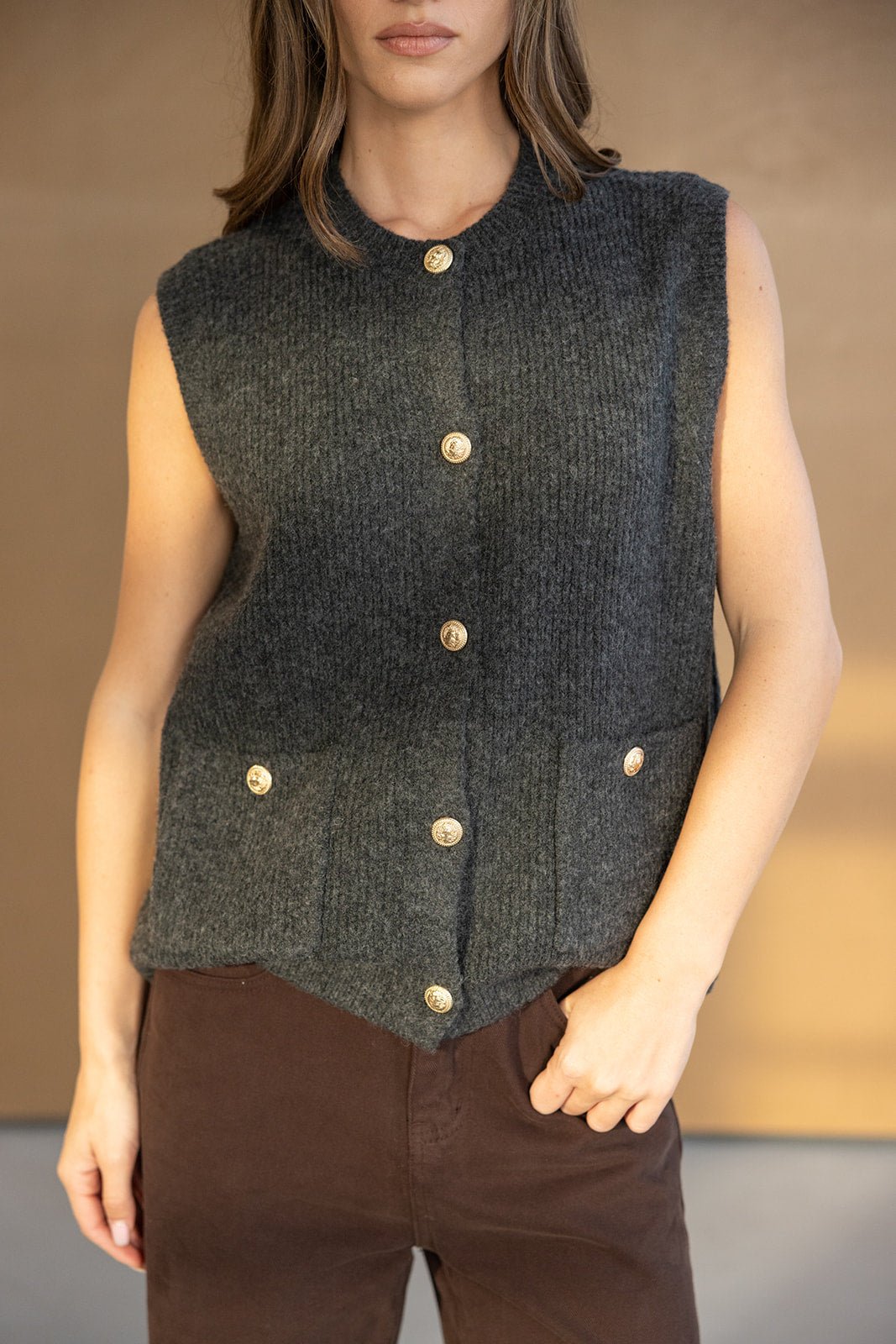 אישה לובשת וסט צמר אפור ללא שרוולים עם כפתורים מוזהבים, אופנה לנשים צעירות