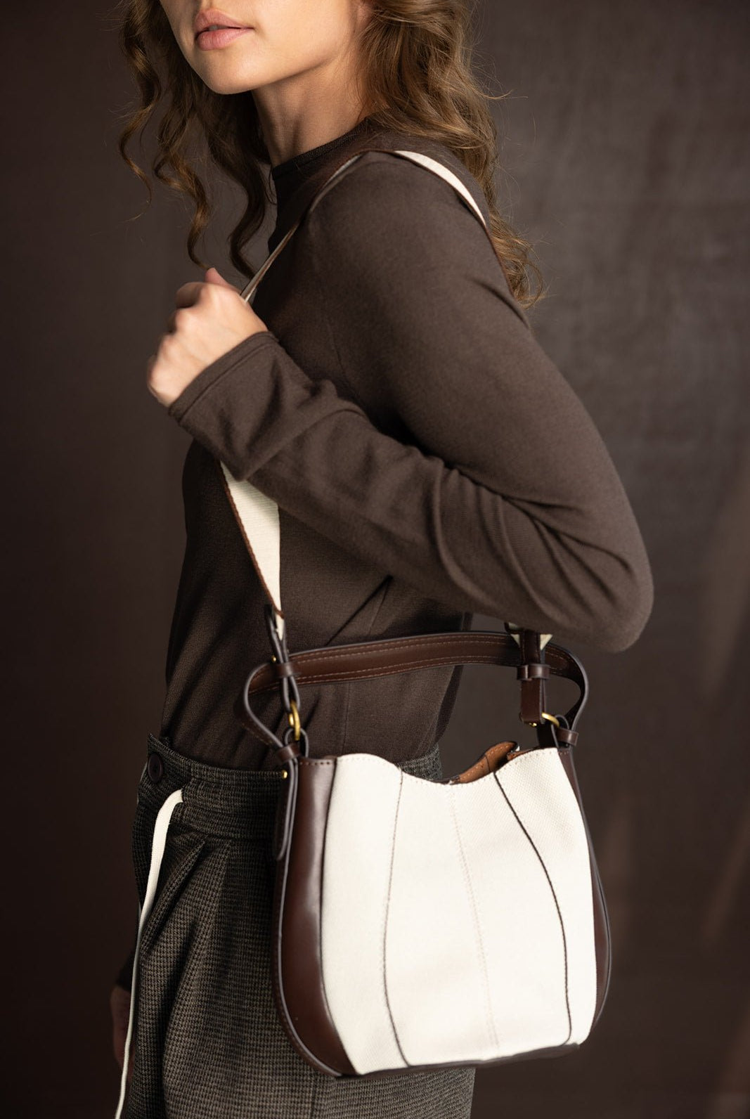 אישה עם חולצה חומה מחזיקה תיק צד אופנתי מבד לבן עם קצוות חומים, רקע כהה