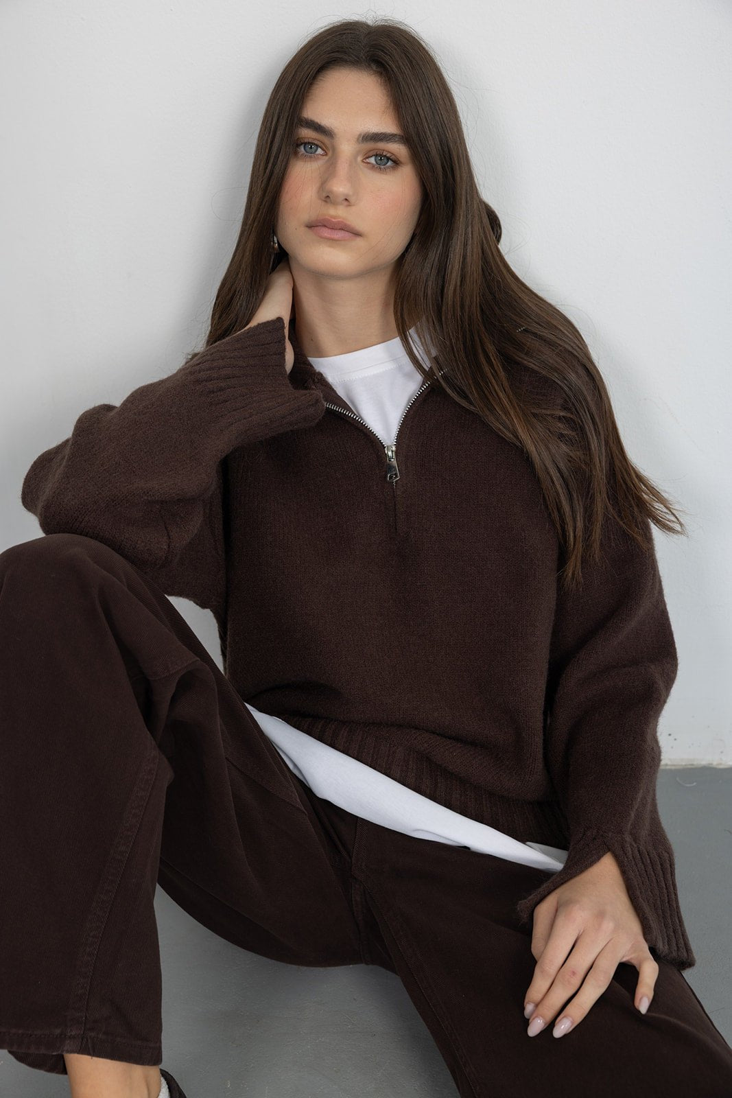 דוגמנית יושבת לובשת סוודר חום עם רוכסן וחולצה לבנה, אופנת נשים צעירה ואופנתית