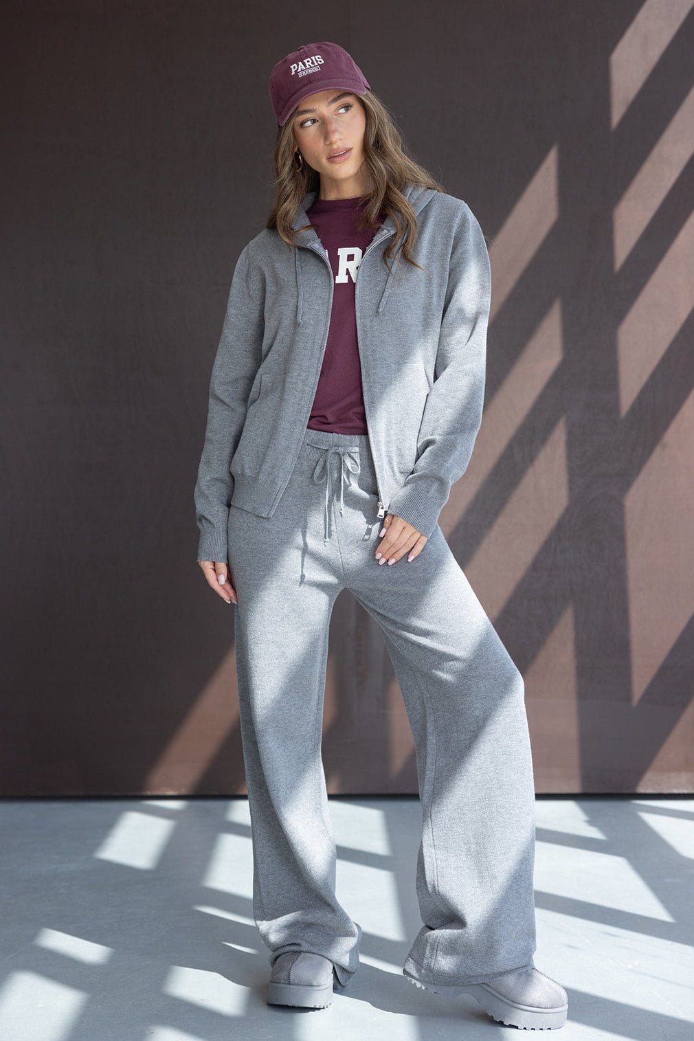 צעירה לובשת סט טרנינג אפור עם קפוצ’ון, חולצה וכובע בורדו, אופנה נינוחה לנשים